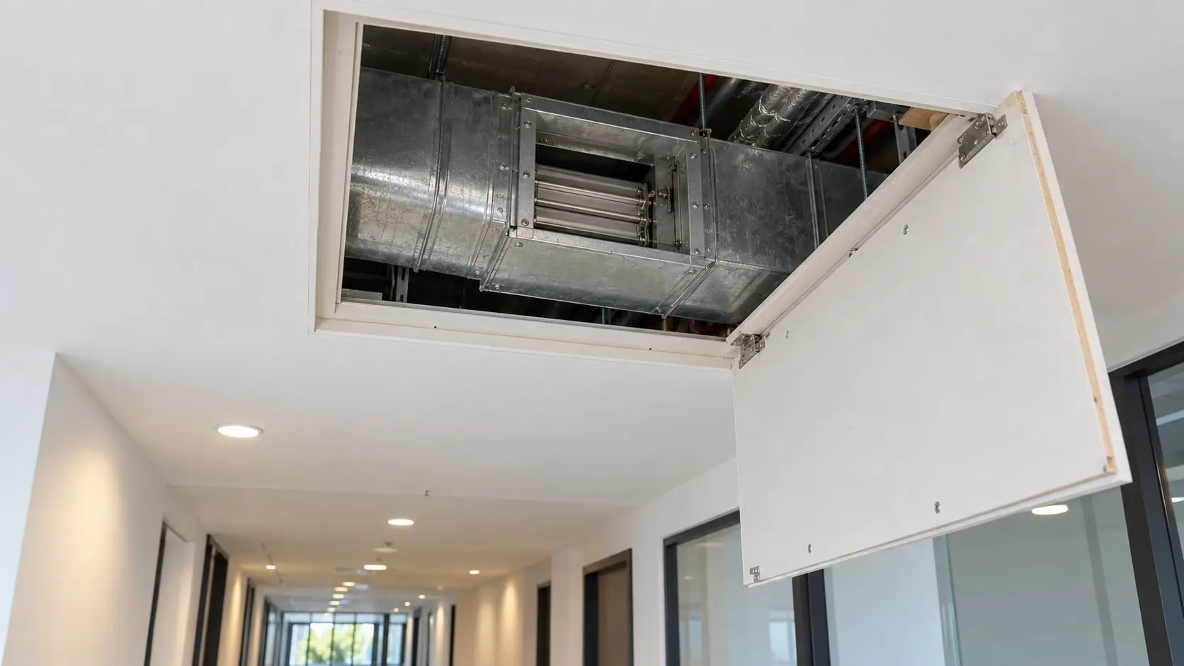 Open ceiling access hatch showing ductwork and a fire damper above a corridor